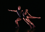 Two ballet dancers wearing black dance together on stage