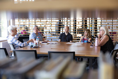 camera peeks thru books on the bookshelf to capture a group of people discussing book club at the SCC