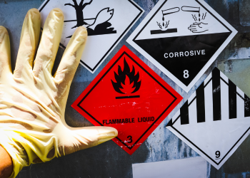 A gloved hand points to stickers reading "flammable liquid" and "corrosive"