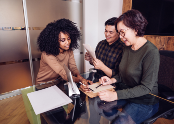 Three employees discuss paperwork at a conference table