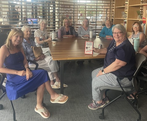 A group of seniors sit around a table at the library during book club