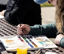 photo of a woman painting with water colors on an outdoor picnic table
