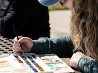 photo of a woman painting with water colors on an outdoor picnic table