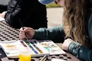 photo of a woman painting with water colors on an outdoor picnic table