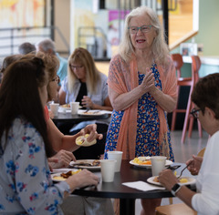 woman talking to two other people at the senior welcome breakfast while others eat in the background behind her