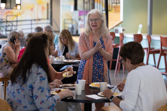 woman talking to two other people at the senior welcome breakfast while others eat in the background behind her