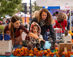 2 women and a young girl pointing at items on a decorated fall table during the farmer's market