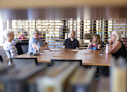 camera peeks thru bookshelf at a group of seniors discussing book club