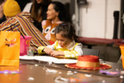 A young girl with pumpkin face paint on her cheek works on a craft at Monster Mash