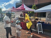 A person in a banana costume talks with guests at a booth a the Summer Market event.