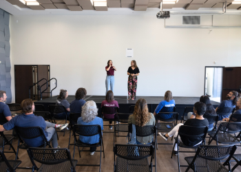 Two people speak on a stage to a crowd at the Superior Civic Space