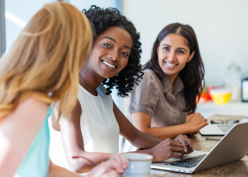Three women smile at each other while working