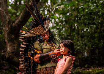 A person in a Native American headdress puts tribal makeup on a young child