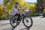 A young person wearing a helmet and riding an e-bike on a sunny day with fall foliage in the background.