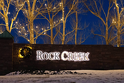 White lights on trees behind the lit up Rock Creek neighborhood sign