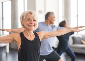 A woman with short blonde hair stretches in warrior position during a yoga classs