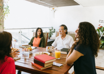 Four people sit around a table with books and drinks 