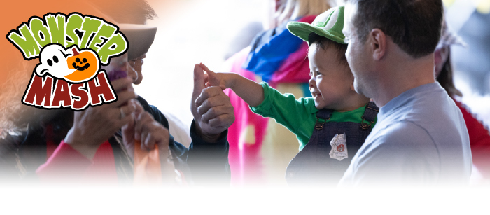 Child in a Luigi costume smiling as they hold their grandpa's thumb.