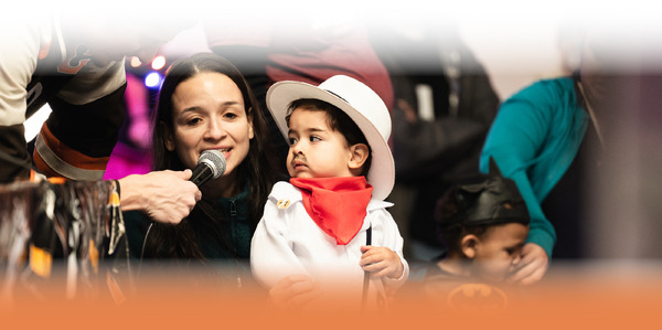 Woman Speaking while child in a cowboy costume watches here intently.