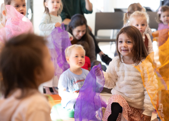 A group of children play with colorful fabric during storytime