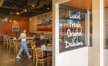 Customers inside a business with "local, fresh, original, delicious" on doors
