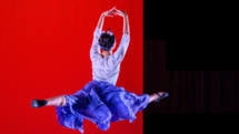 A ballerina dances on a stage with a red and black background
