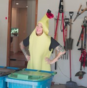 A person in a yellow banana costume poses in front of a compost cart