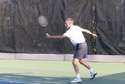 A man in a white shirt and gray shorts goes for a ball while playing tennis