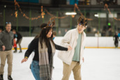 Two people wearing festive holiday accessories ice skating at the 2024 Winter Festival 