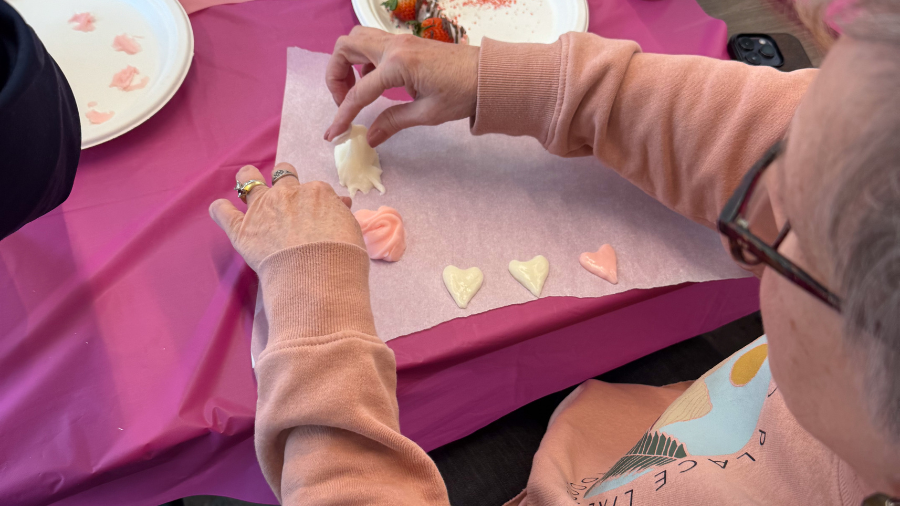 A woman in a pink sweatshirt makes pink and white candy hearts