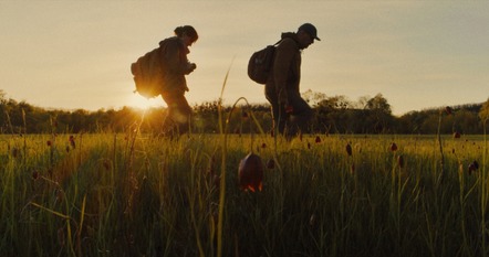 Two people walking through a field of wilted flowers. 