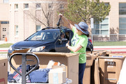 A woman in a green shirt digs through a box of electronics and other hard-to-recycle items