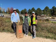 Three Weed Warriors volunteers stand with a bag of weeds pulled from a park