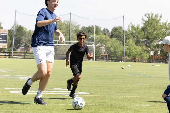 A young soccer player chases the ball next to a Marcello camp counselor