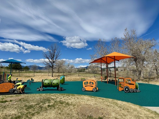 Five people at work on the Community Park Playground. They are wearing yellow shirts and are working with tools.