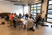 A group of people sit in a circle and practice playing ukulele