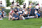 A crowd of people sit in the grass during the Summer Concert Series