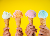 Four hands hold colorful ice cream cones on a yellow background