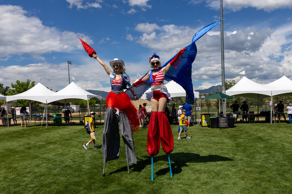 Two women smile for the camera while dressed in red, white, and blue and walking on stilts at the 4th of July Celebration