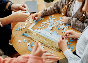 Four people complete a puzzle on a table