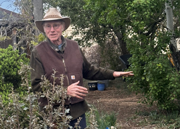 Mikl Brawner wearing a felt hat and gesturing to a path with mulch on the ground.