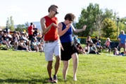 A person in a red shirt and a person in a blue shirt dance together in the grass during a Summer Concert Series event