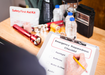 A hand holding a pencil checks off items on an emergency preparedness checklist