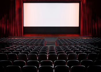 Empty theater with black seats, red curtain, stage and white movie screen