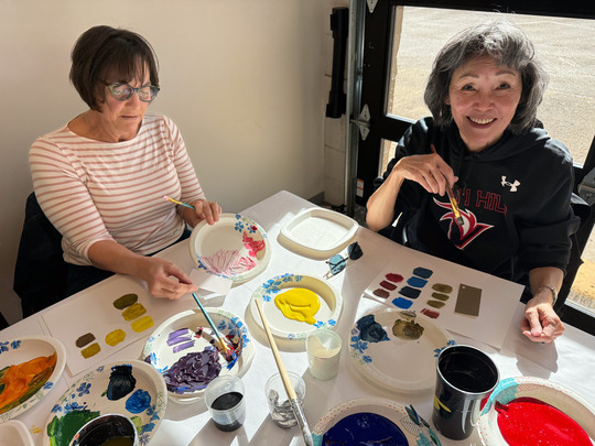 Two people smile while painting at the community center