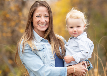 A woman with long brown hair and a child with blonde hair smile for a photo
