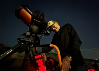 A man in a hat smiles while looking into a telescope during a Superior stargazing event