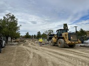 Two construction workers in yellow vests stand near a bulldozer at the Superior Community Center.