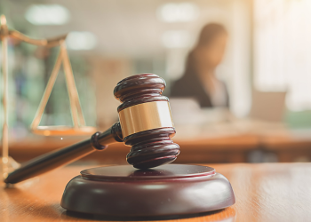 Gavel with scales of justice in the background and a silhouette of a person.