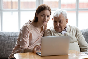 Adult daughter and her older father look at a laptop together